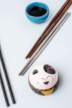 Image with wooden and metal Asian chopsticks, a small container with soybeans and a smiling ceramic anime catの写真素材