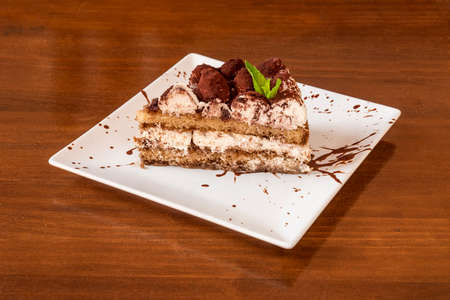 wonderful and provocative portion of Italian tiramisu cake with chocolate truffles on top, chocolate syrup, cream in abundance on a square white plateの写真素材