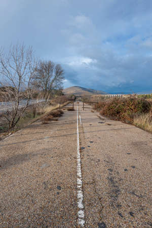 Old mountain road cut in the direction of passing under an aqueduct on a cloudy day threatening rainの写真素材