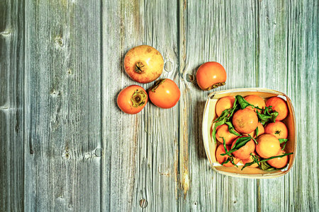 Top view image of wooden basket with ripe fruit, mandarinas with green leaves, persimmons and...