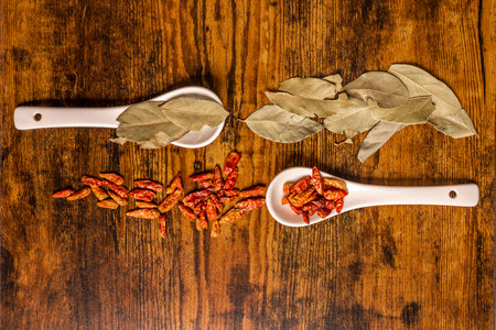porcelain spoons with cayenne and bay leaves on dark wooden tableの写真素材