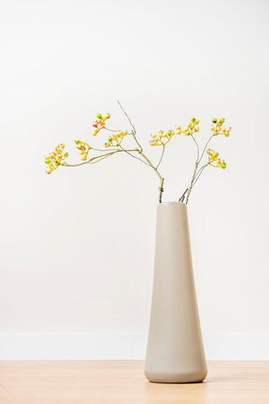 Long gray vase with decorative immature blueberry branches on wooden floor and white background
