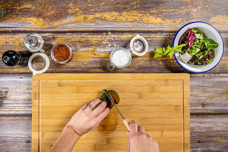 Top view image of female chef's hands with ring cutting a tomato on a bamboo table to prepare a...