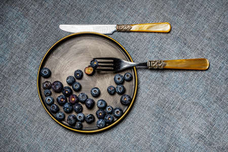 Top view image of vintage plate and cutlery with blueberries on gray clothの写真素材