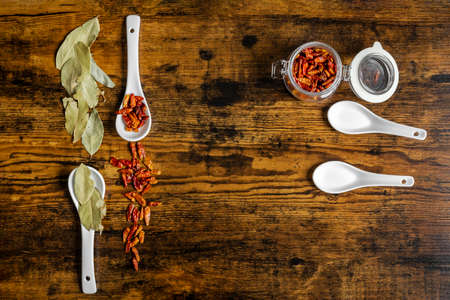 Top view image of white porcelain spoons with cayenne and bay leaves on dark wooden tableの写真素材