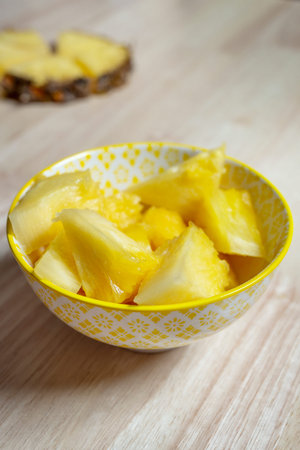 nice yellow bowl filled with pieces of delicious yellow pineapple on light wooden tableの写真素材