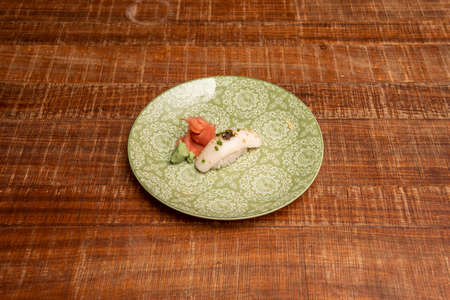 Delicious bite of butterfish sushi nigiri with wasabi and ginseng with fish roe on a beautiful green plate on a wooden tableの写真素材
