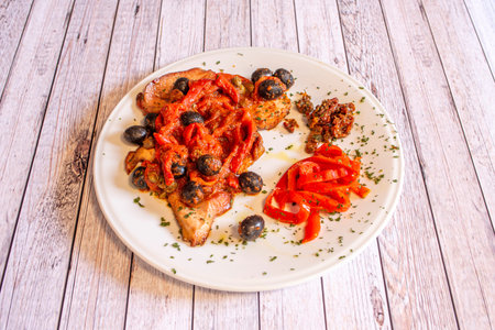 Veal escalopes with black olive sauce and red peppers with chopped fresh parsleyの写真素材