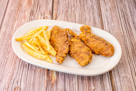 Breaded chicken schnitzels garnished with homemade french fries on a white trayの写真素材