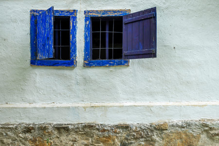 Old blue wooden windows in a whitewashed wall with rubble on the stone base