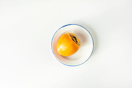 Ripe persimmon on white plate with blue border