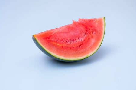 Piece of red watermelon without seeds resting on its green rind on blue backgroundの写真素材