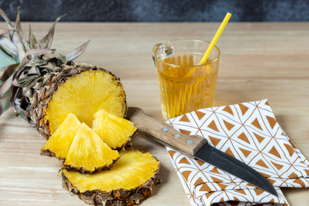 Pineapple cut in half and pineapple chunks on top, pineapple juice in a glass and knife on a cloth
