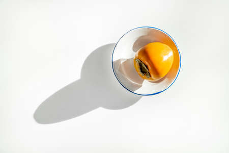 Ripe persimmon on white plate and long shadow on white tableの写真素材