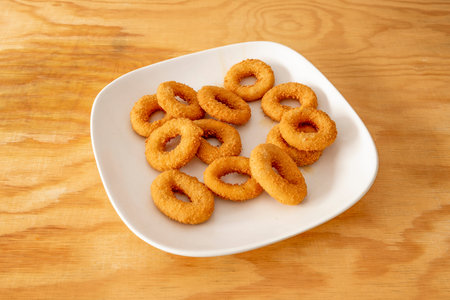 Onion rings battered with flour, egg and breadcrumbs fried in olive oil on pine wood table