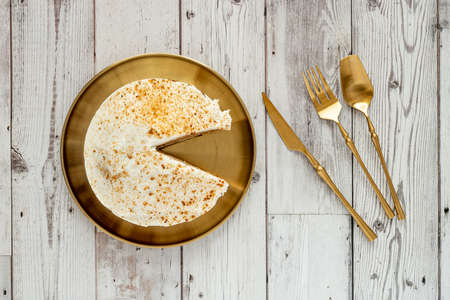 Top view image of carrot cake without a piece on golden metal plate and golden cutlery on wooden tableの写真素材