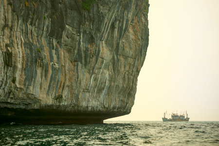 Vertical walled island in the waters of the Andaman Sea with some fishing boats in the background