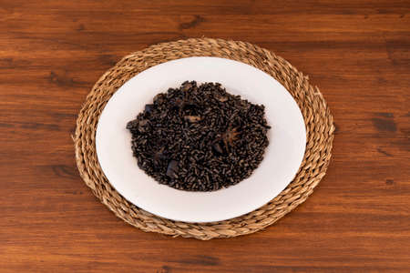 Black rice paella with prawns and squid on a white plate and rattan trivetの写真素材