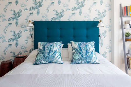 Blue fabric headboard with cushions and blue patterned wallpaper in a king size bedroom in a vacation rental apartmentの写真素材