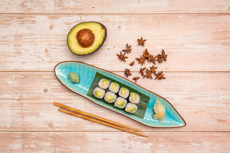 Top view image of a serving of Japanese maki sushi stuffed with white rice and ripe avocado wrapped in nori seaweed with half an avocado with seeds and chopsticksの写真素材