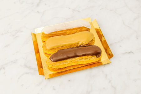 Tray of eclairs with topping of three different chocolates on white marble tableの写真素材
