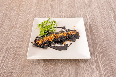 Ravioli stuffed with fish with squid ink sauce and arugulaの写真素材