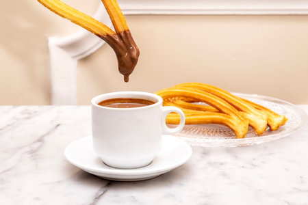 Madrilenian breakfast churro dipped in hot milk chocolate on white marble tableの写真素材