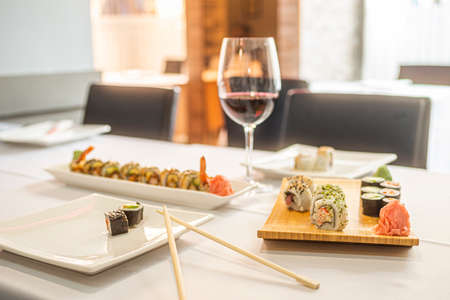 sushi uramaki roll with ginseng and wasabi, chopsticks and glass of wine in a restaurant with white tableclothの写真素材