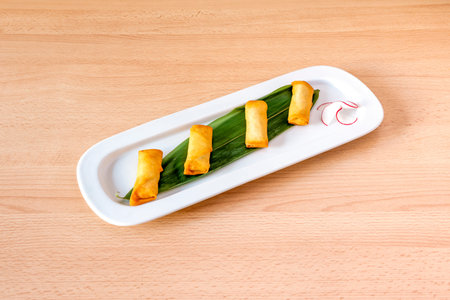 Crispy fried vegetable rolls on a banana leaf on a white tray