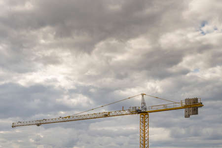 yellow building construction crane with counterweights on a cloud filled dayの写真素材