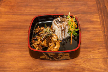 Beef cooked in a Chinese restaurant with sauteed mushrooms and bamboo, bean sprouts, white rice and teriyaki sauce on a traditional wooden plateの写真素材