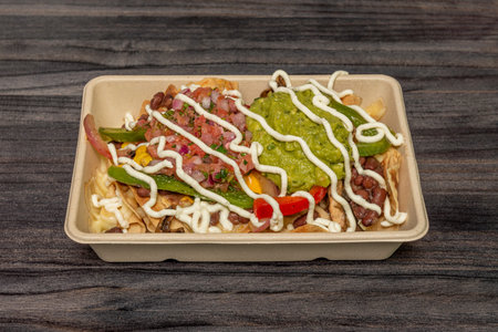 takeaway container with nachos with guacamole, red beans, pico de gallo, peppers and tomato and corn...