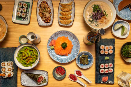 Japanese food dishes with assorted sushi, gyozas, dumplings, octopus takoyaki, red tuna temaki, edamame in pods, hosomaki, red pepper, matcha truffles, nori seaweed and wakame seaweedの写真素材