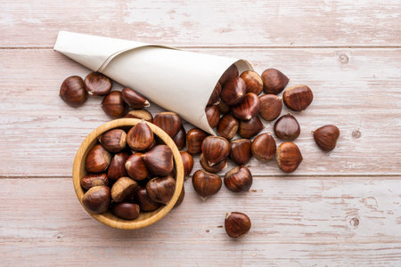 Chestnut cornet and wooden bowl with chestnuts on a light wooden tableの写真素材