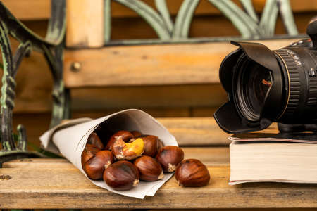 A cornet of roasted chestnuts in front of a camera lens on a wooden benchの写真素材