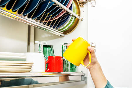 Man's hand putting a yellow mug in the kitchen cupboard to drain the dishesの写真素材