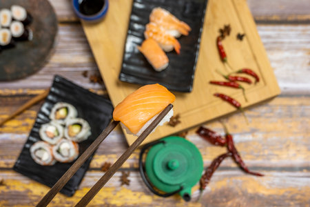 Wooden chopsticks holding a Japanese Norwegian salmon nigiri and sushi plates in the backgroundの写真素材