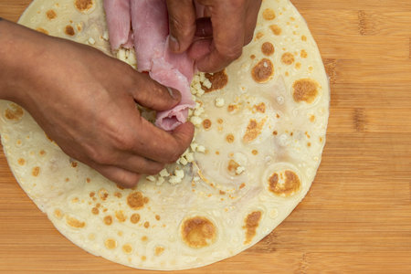The chef placing the cooked ham with his hands over chopped fresh cheese inside a salty crepe