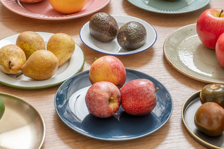 Plates with apples, with avocados, group of plates with pears and tomatoes on wooden table