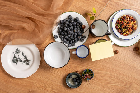Still life with enameled and fine porcelain plates with blueberries, plants, yellow note and nutsの写真素材