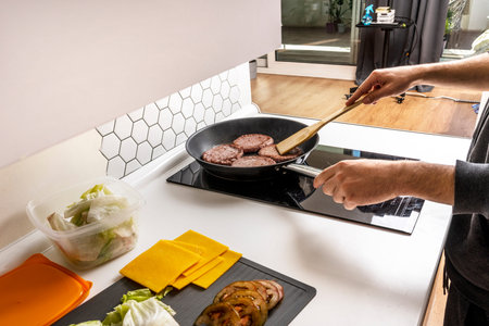 Hands of young man cooking beef burgers in a frying pan with their seasonings to fill the bread