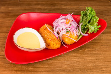 Peruvian style croquettes with chili sauce and raw red onion in quantity on a red plate