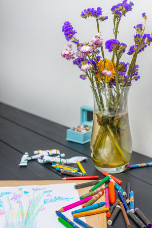 Vase with dried flowers, cream paints and colored pencils on black tableの写真素材