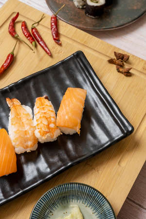 Black tray with Norwegian salmon nigiri sushi and spicy cooked prawns on a bamboo tableの写真素材
