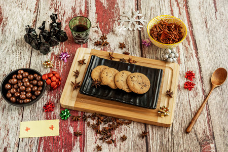 Chocolate cookies on a black plate with star anise and a plank board with red and white colors.