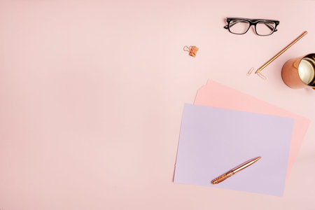 Still life top view of writer in pastel pink tones with copper jug, black glasses and papersの写真素材