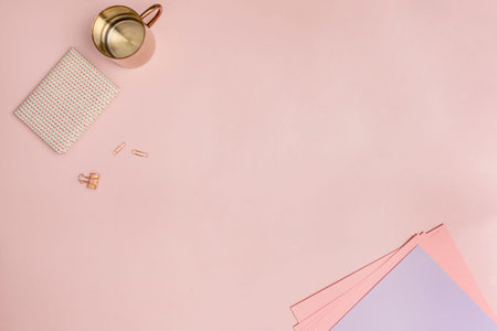 Still life top view of writer in pastel pink tones with copper jug, notepad, clips and papers