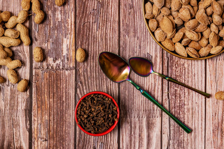 Still life top view of almonds, iridescent spoons, peanuts and spice cloves
