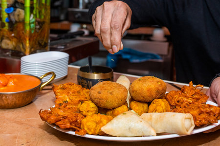 Chef's hands seasoning a tray of assorted Hindu appetizers in a restaurant