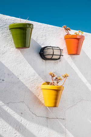 Pots of different colors with glitter on a whitewashed wall and a pristine blue skyの写真素材